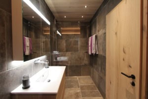 Zeitgemäßes Badezimmer mit Holz- und Steinoptik, moderner Beleuchtung und Doppelwaschbecken.