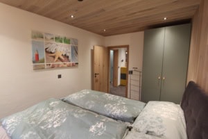 Gemütliches Schlafzimmer mit Doppelbett, Holzdecke und Blick auf den Flur.