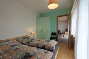 Gemütliches Schlafzimmer mit Bett, Kleiderschrank und Blick ins Wohnzimmer.