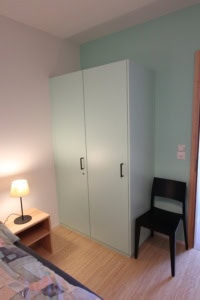 Schlafzimmer mit weißem Kleiderschrank und schwarzem Stuhl.