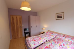 Gemütliches Schlafzimmer mit Doppelbett, Wandlampe und Kleiderschrank.