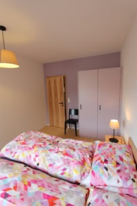 Modernes Schlafzimmer mit buntem Bettzeug, Kleiderschrank und Nachttischlampe.