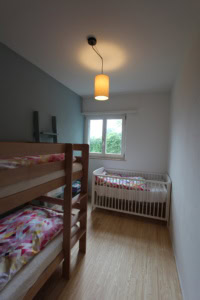 Helles Kinderzimmer mit Etagenbett und Kleinkindbett, Blick auf Fenster und Natur.