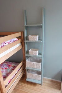 Helles, blaues Bücherregal mit mehreren Körben neben Kinderbett.