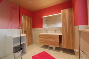 Helles Badezimmer mit Holzschränken und rotem Akzentwand.