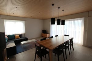 Geräumiges Wohnzimmer mit Esstisch, Sofa und großen Fenstern.