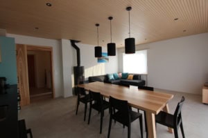 Helles Esszimmer mit Holzdecke, schwarzer Kamin und großem Tisch.