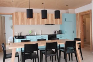Moderne Küche mit Essbereich, blaue Schränke, Holzdecke, schwarze Lampen.