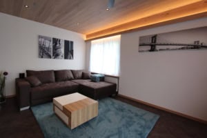 Gemütliches Wohnzimmer mit braunem Sofa, Holzdecke und Kunstwerken an der Wand.