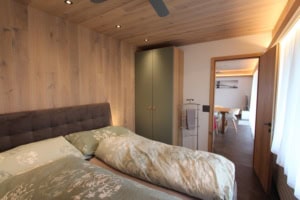 Gemütliches Schlafzimmer mit Holzdecke und Blick ins Wohnzimmer.