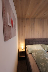 Modernes Schlafzimmer mit Holzdecke und Bett mit grünem Bettzeug.