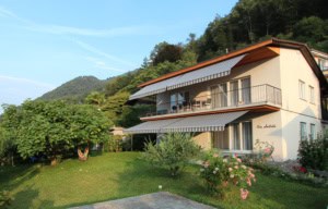 Modernes Haus mit Balkon und Garten in grüner Umgebung.